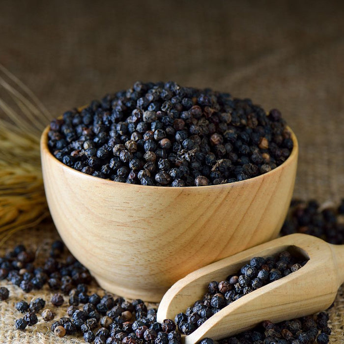 Wooden bowl and scoop filled with black peppers on burlap.