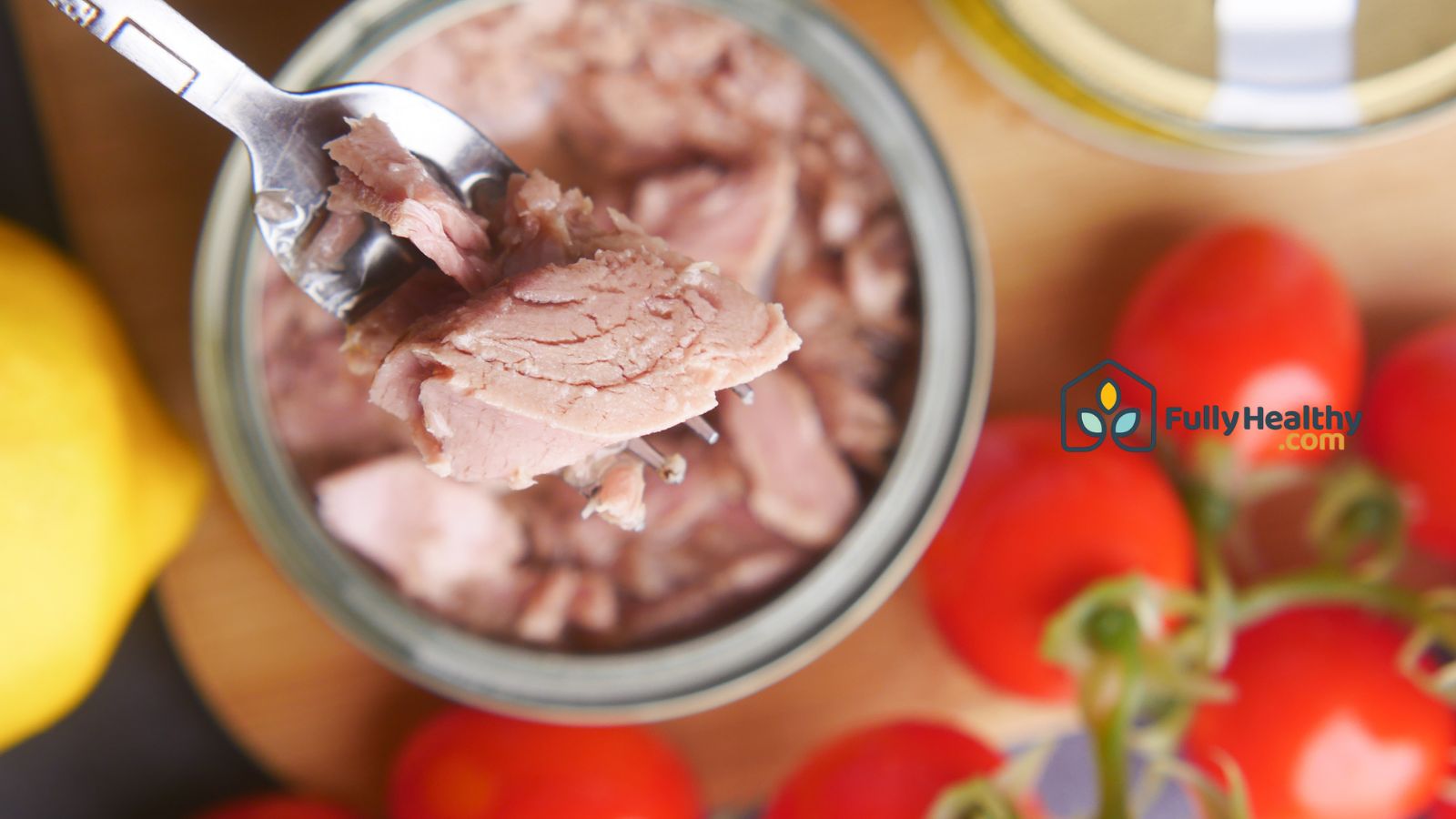Canned tuna in bowl with fork and fresh tomatoes on table