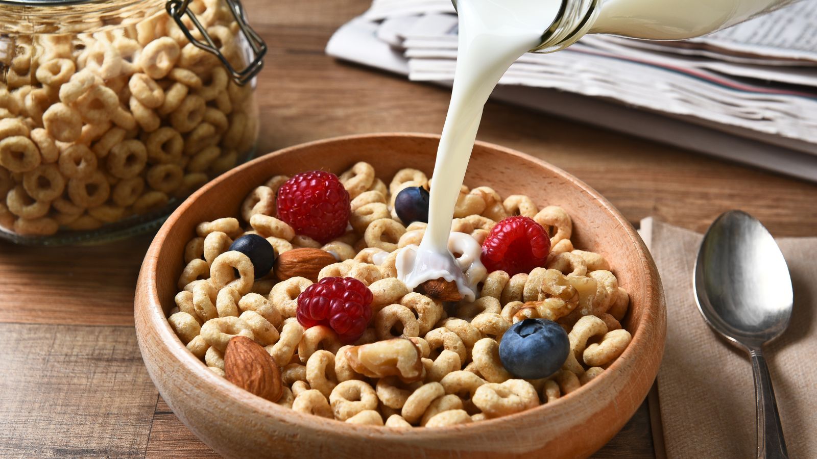 Milk pouring into a bowl of cereal with berries and mixed nuts.