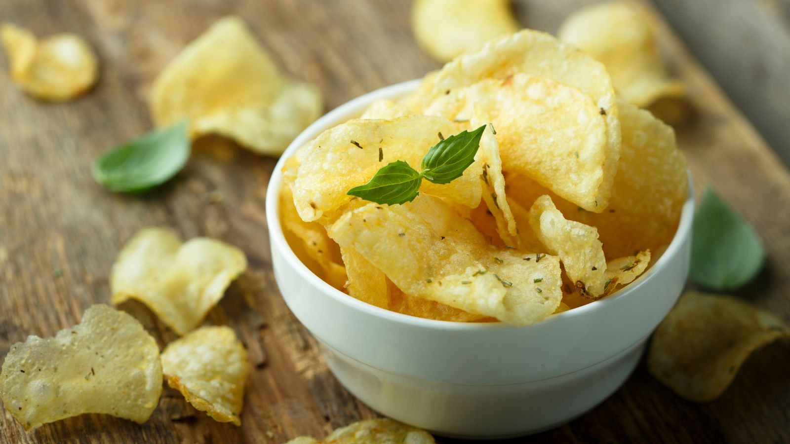 Crispy, herb-seasoned potato chips in a white bowl on a rustic wooden surface.