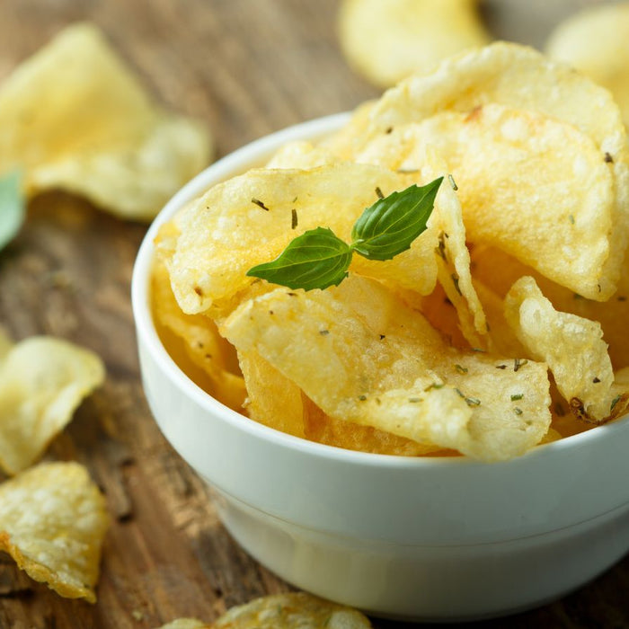Crispy, herb-seasoned potato chips in a white bowl on a rustic wooden surface.