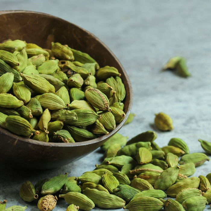 Fresh green cardamom pods in a wooden bowl on a gray surface.