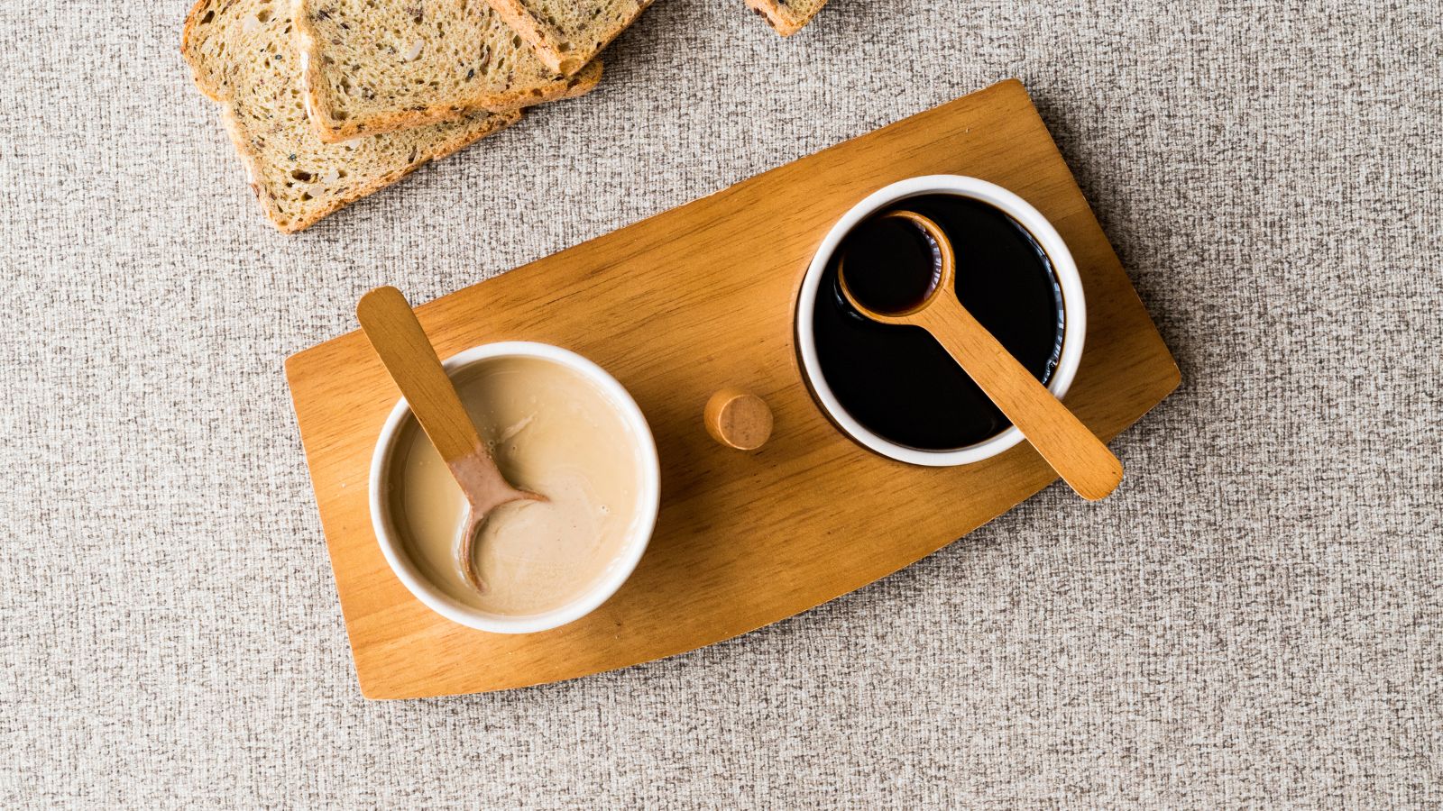 Wooden board with tahini and molasses in bowls with bread slices.