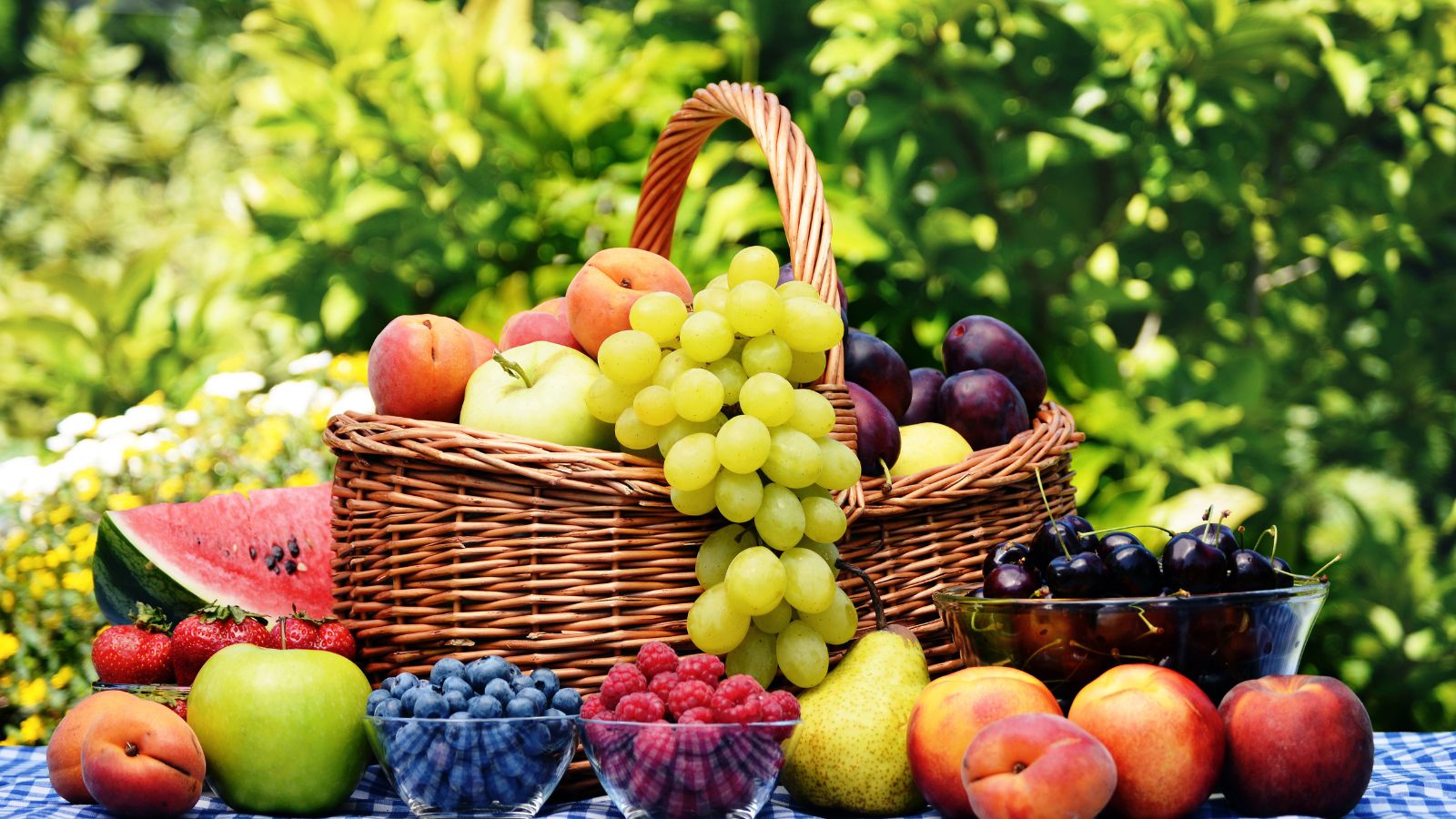 Wicker basket filled with grapes, peaches, apples and cherries on table.