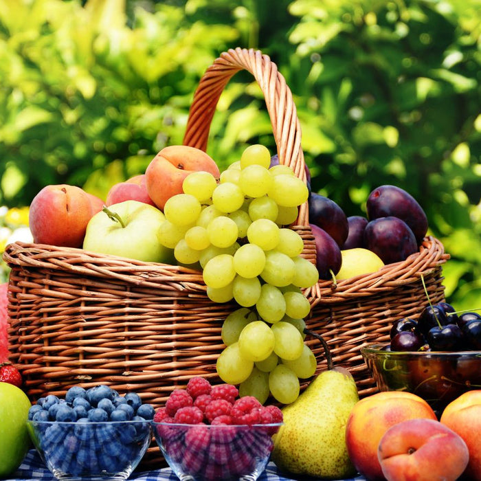 Wicker basket filled with grapes, peaches, apples and cherries on table.