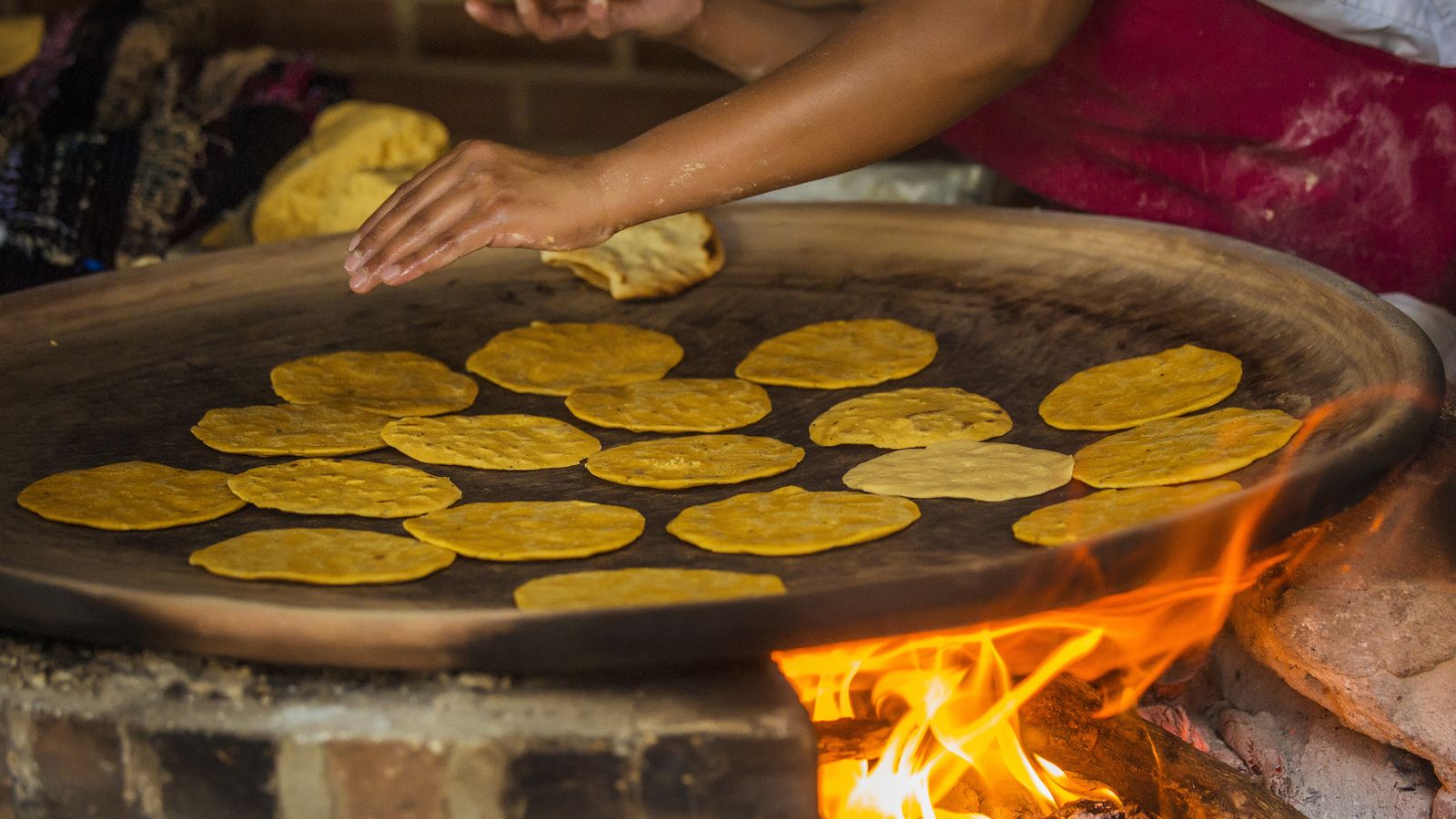 Hand cooking corn tortillas on a traditional wood-fired flat griddle