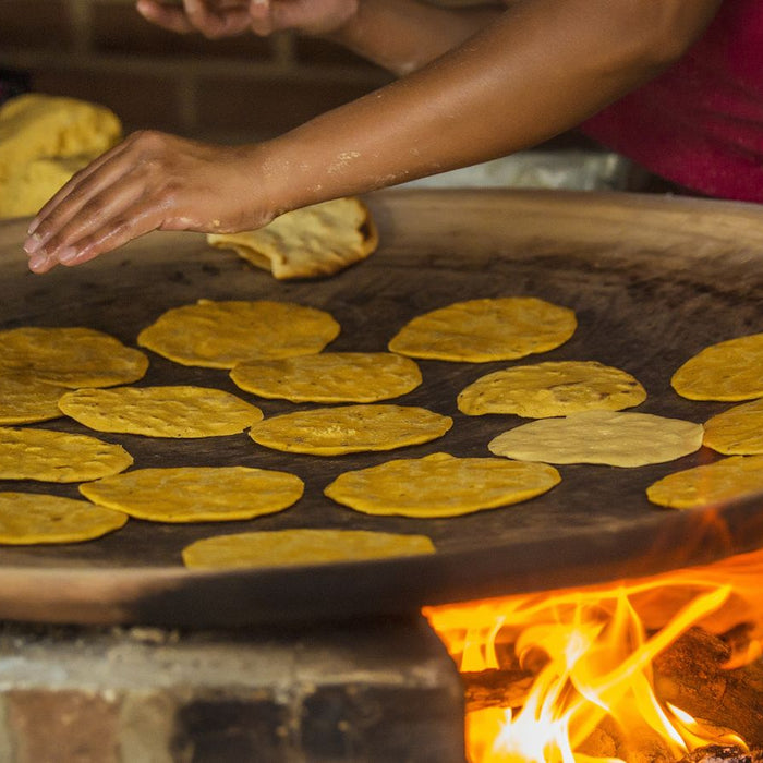 Hand cooking corn tortillas on a traditional wood-fired flat griddle