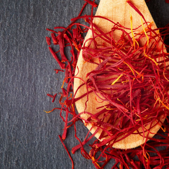 Wooden spoon filled with deep red saffron threads on slate table.