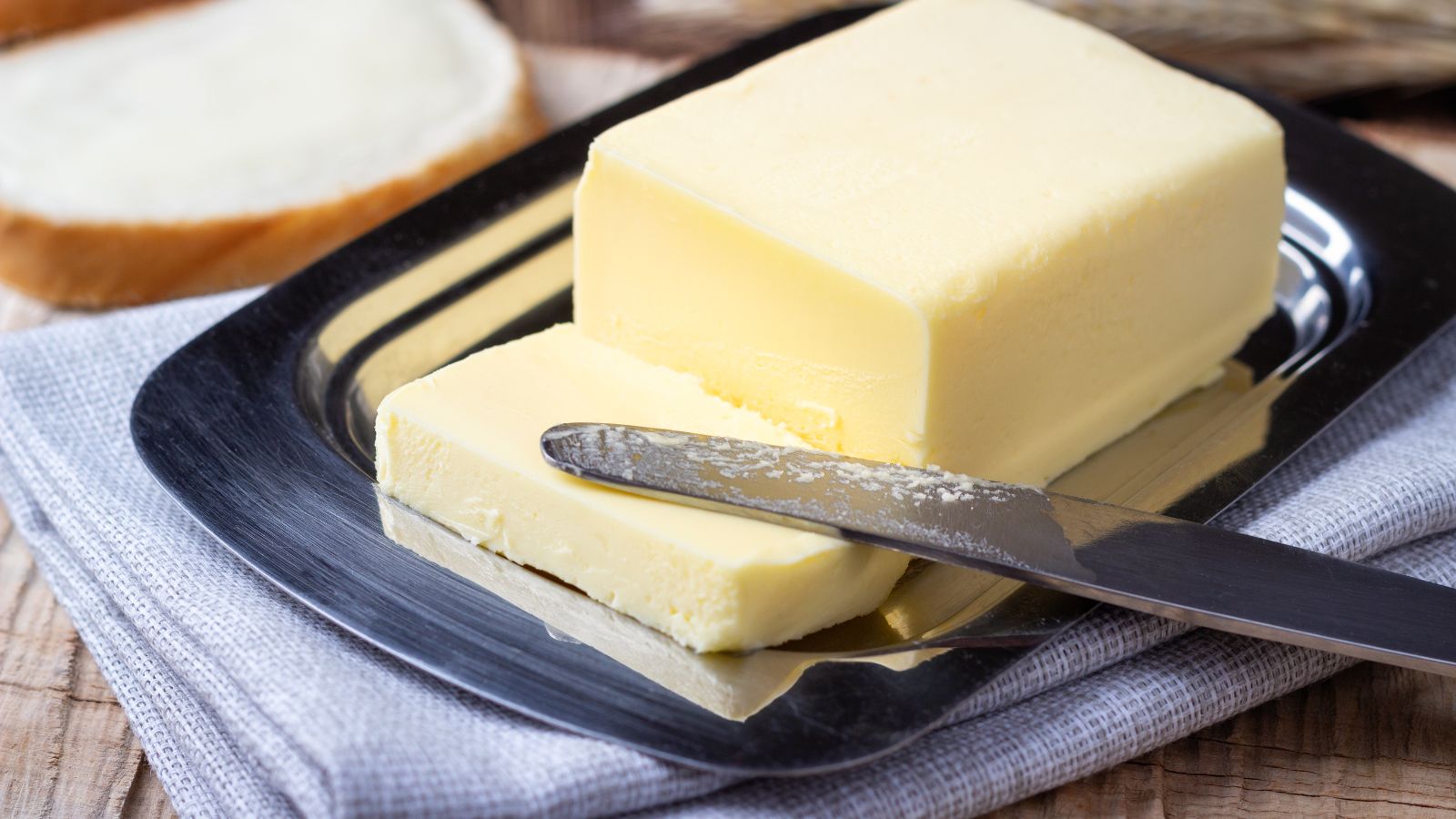Butter curl on a knife beside a block of butter on a tray.