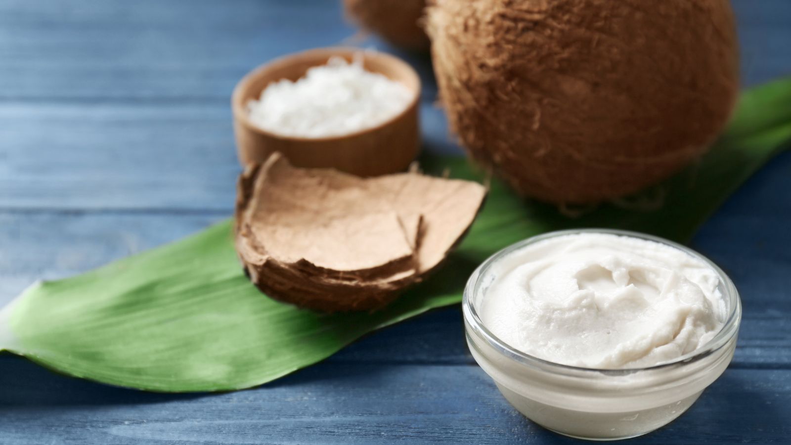 Fresh coconut cream in glass bowl with coconuts and leaf background