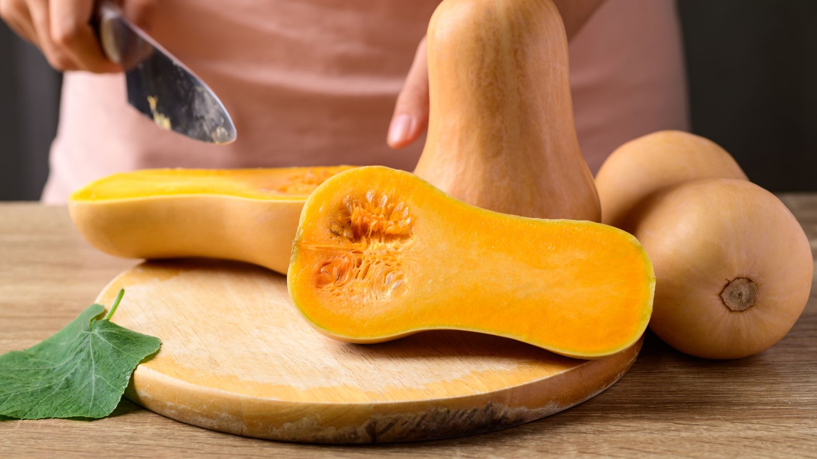 Person cutting fresh butternut squash on wooden board