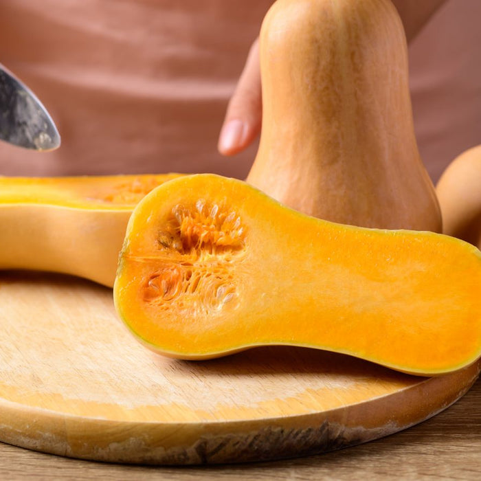 Person cutting fresh butternut squash on wooden board