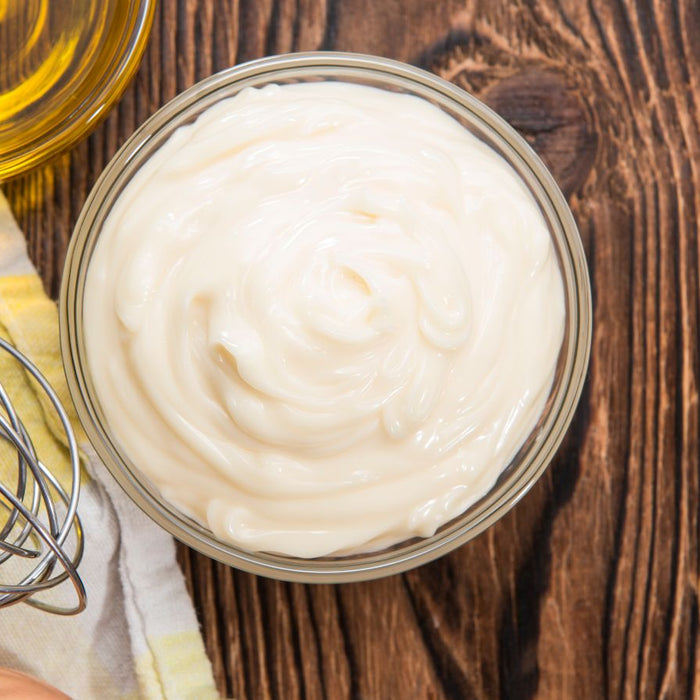 Freshly made mayonnaise in a bowl with whisk and oil on a wooden table.