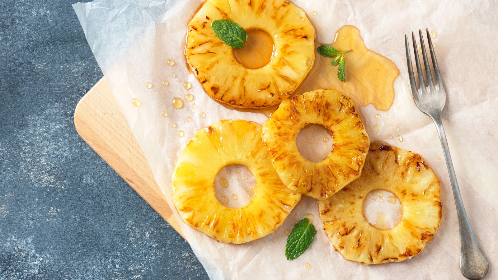 Grilled pineapple rings drizzled with syrup and mint leaves.
