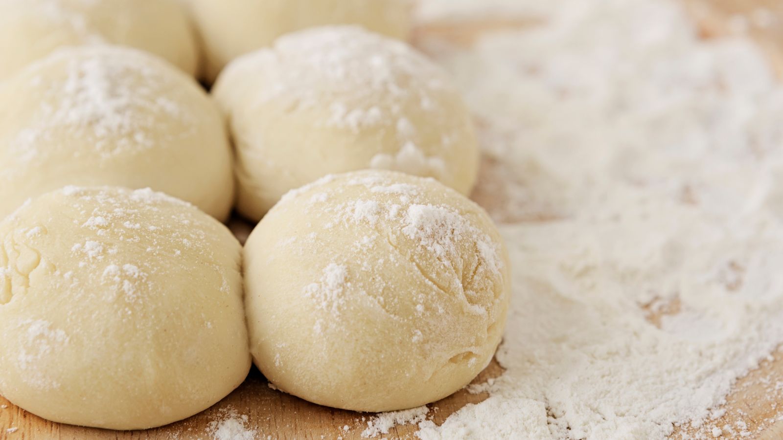 Dough balls covered in flour on wooden surface.