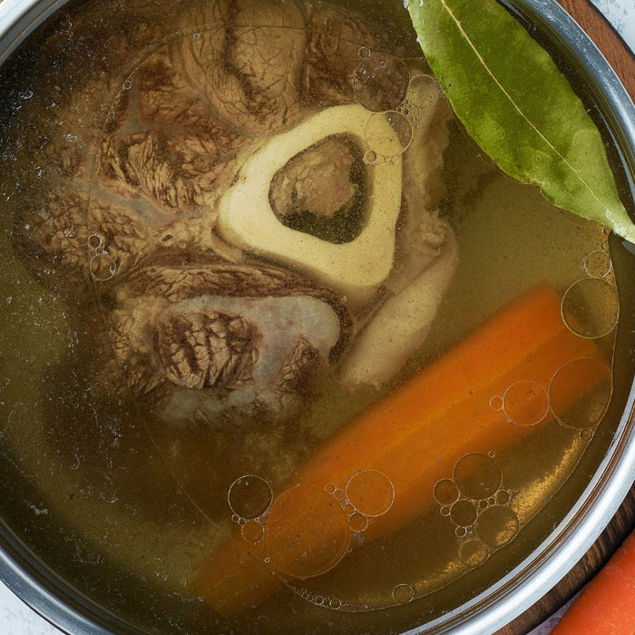 Pot of bone broth with beef marrow, carrots, garlic, and bay leaf.