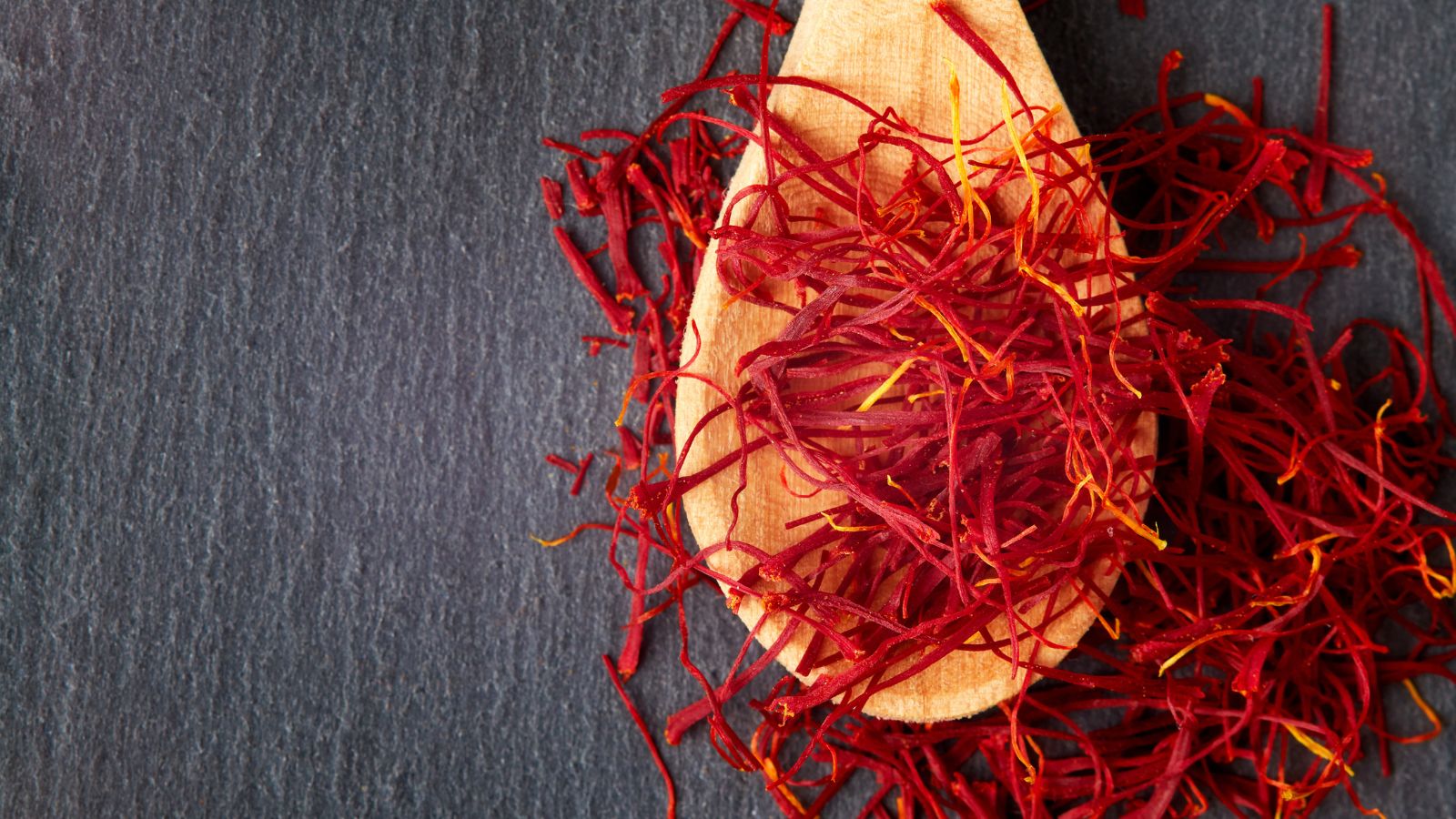 Wooden spoon filled with deep red saffron threads on slate table.