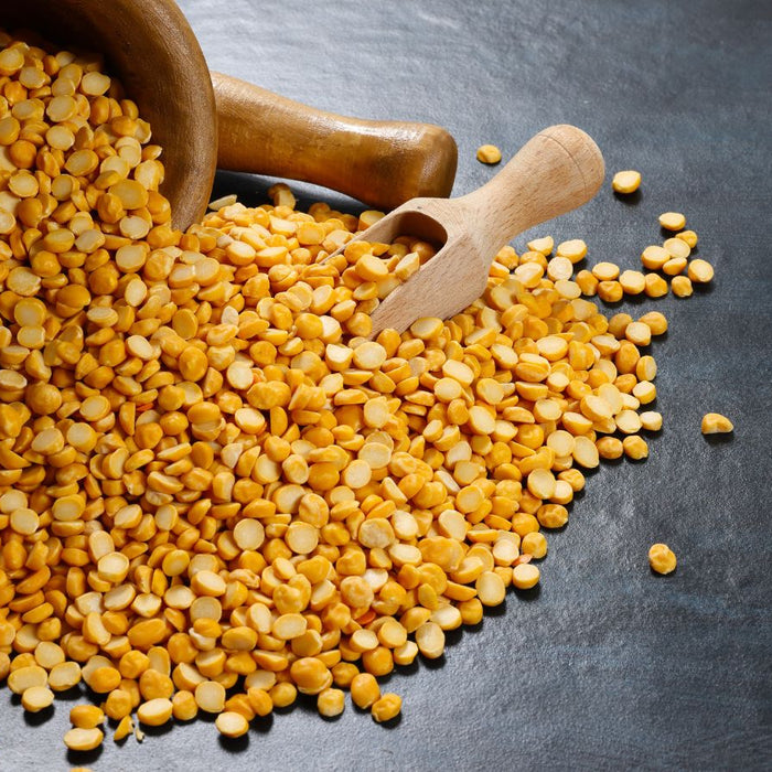 Yellow lentils spilled from a wooden bowl onto a dark surface.