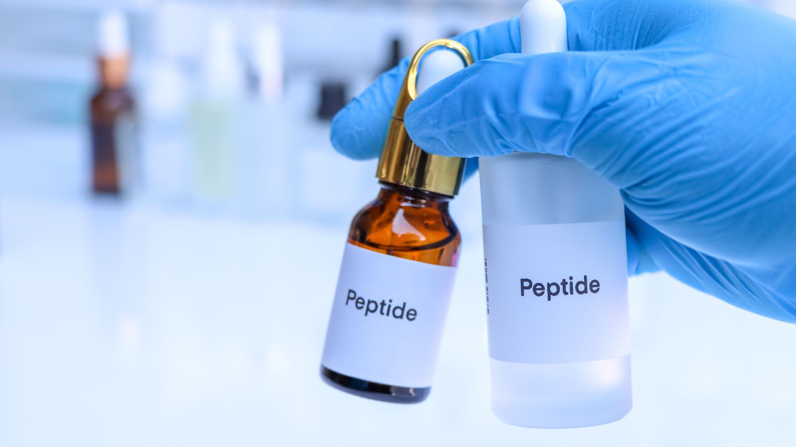 Peptide bottles held by gloved hand in lab setting.
