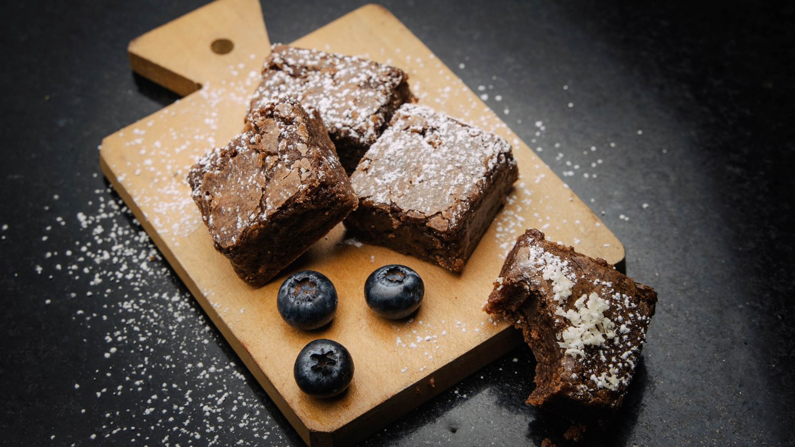 Brownies with powdered sugar and blueberries on wood board