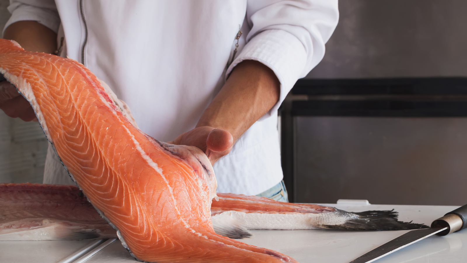Chef filleting fresh salmon on a white cutting board in kitchen.