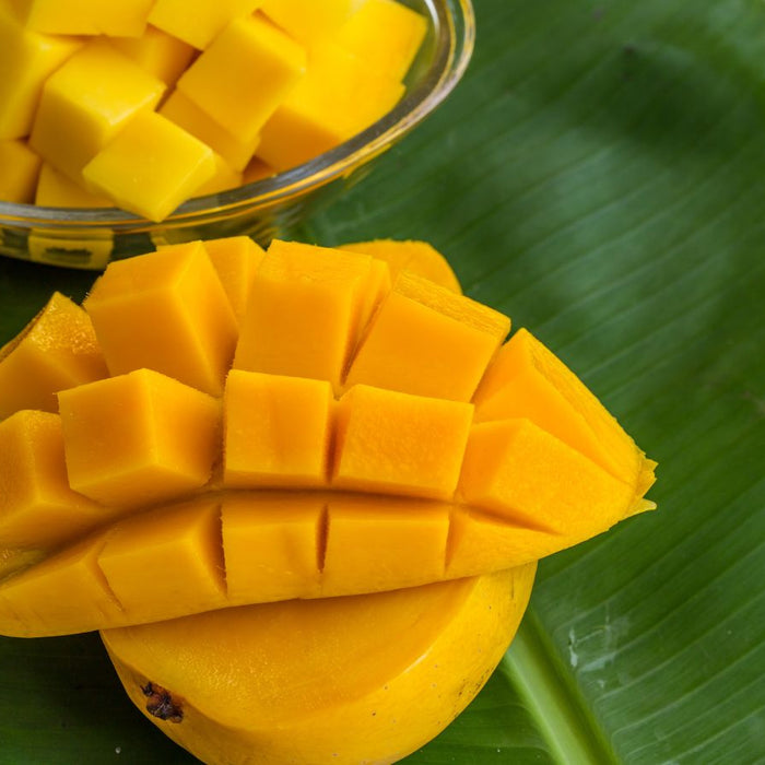 Diced mango cubes in glass bowl on large green banana leaf surface.