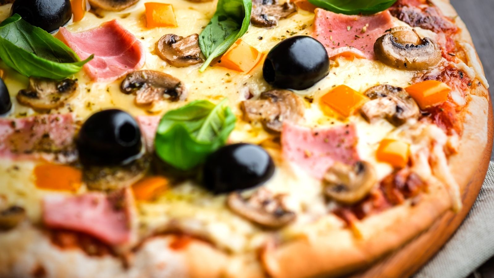 Pizza with olives, mushrooms, ham, cheese, and fresh basil leaves.