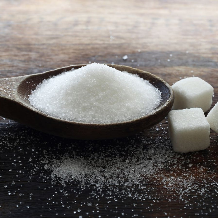 White sugar on wooden spoon with sugar cubes on rustic table.