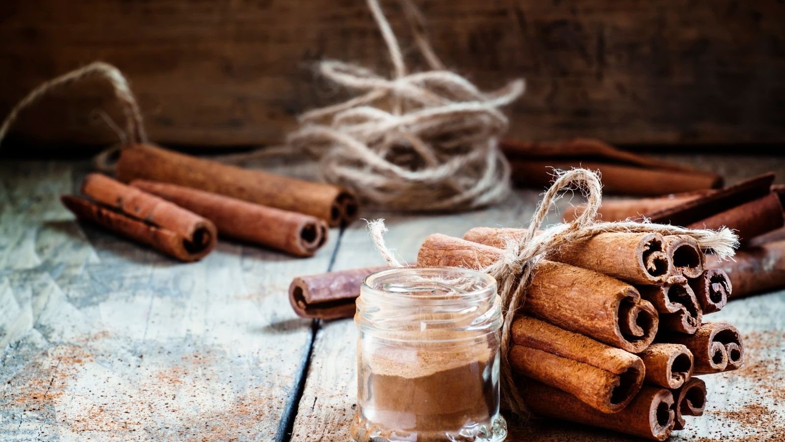 Jar of cinnamon powder and tied sticks on rustic table.