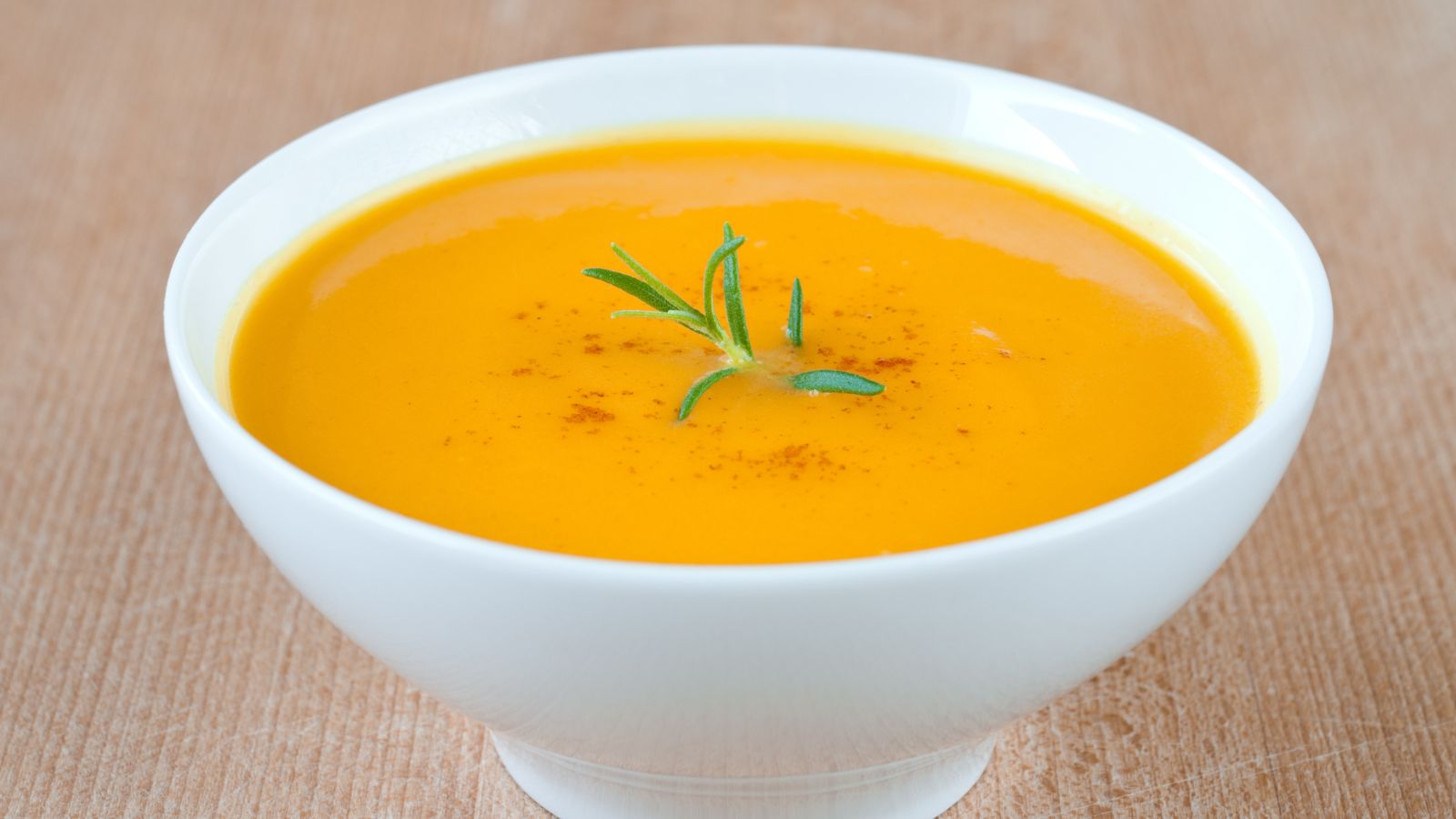 Creamy vegetable soup garnished with rosemary in a white bowl