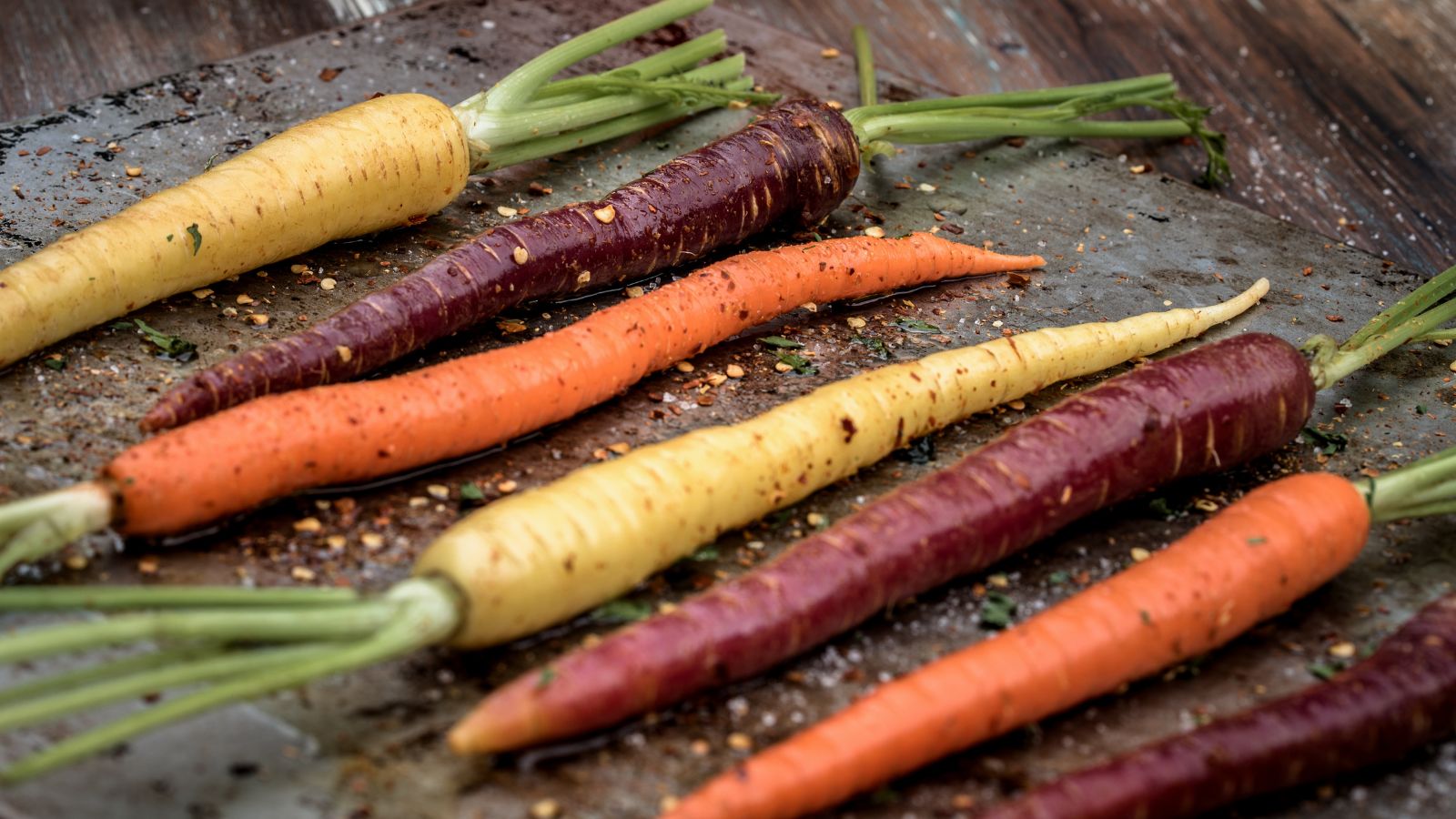 Seasoned heirloom carrots in purple, orange, and yellow on baking sheet.