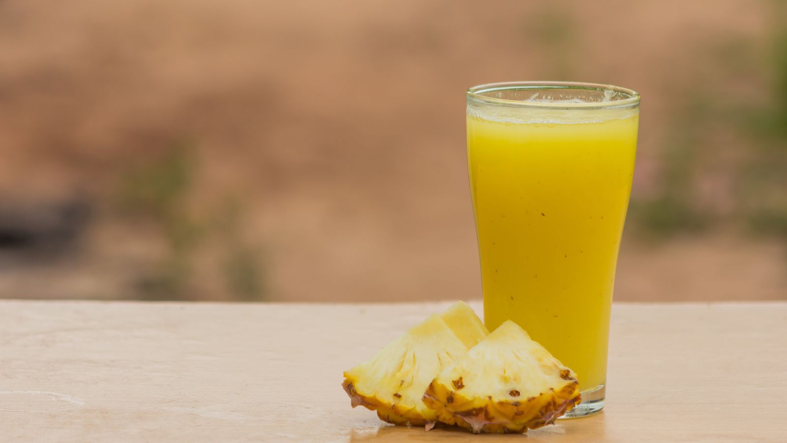 Glass of fresh pineapple juice with slices on wooden table.