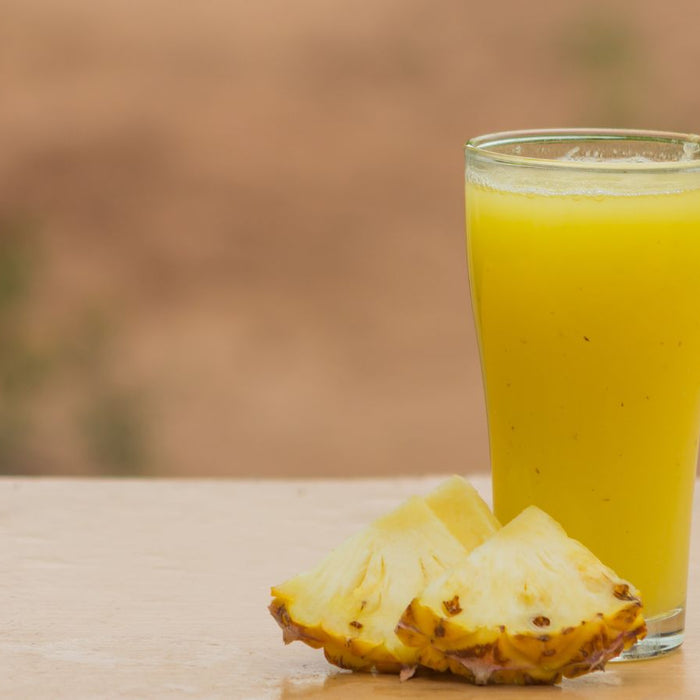 Glass of fresh pineapple juice with slices on wooden table.