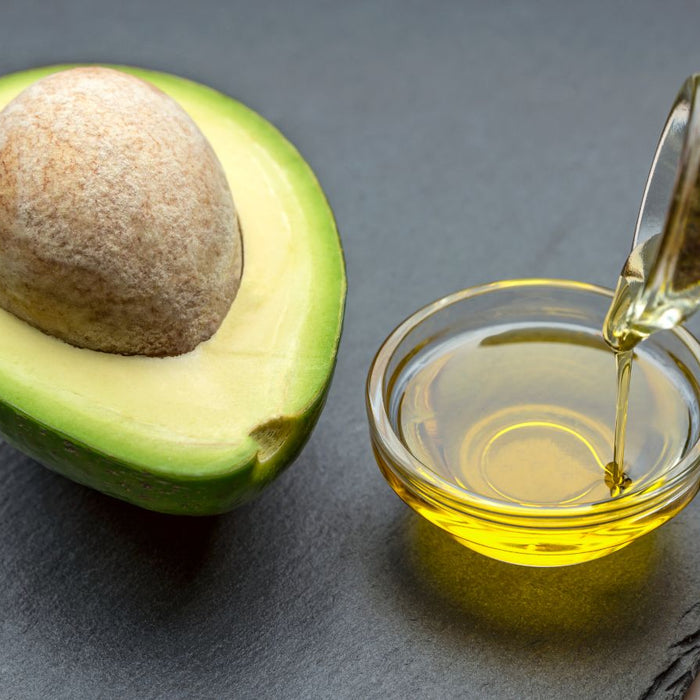Avocado half with seed and avocado oil being poured in a glass bowl.