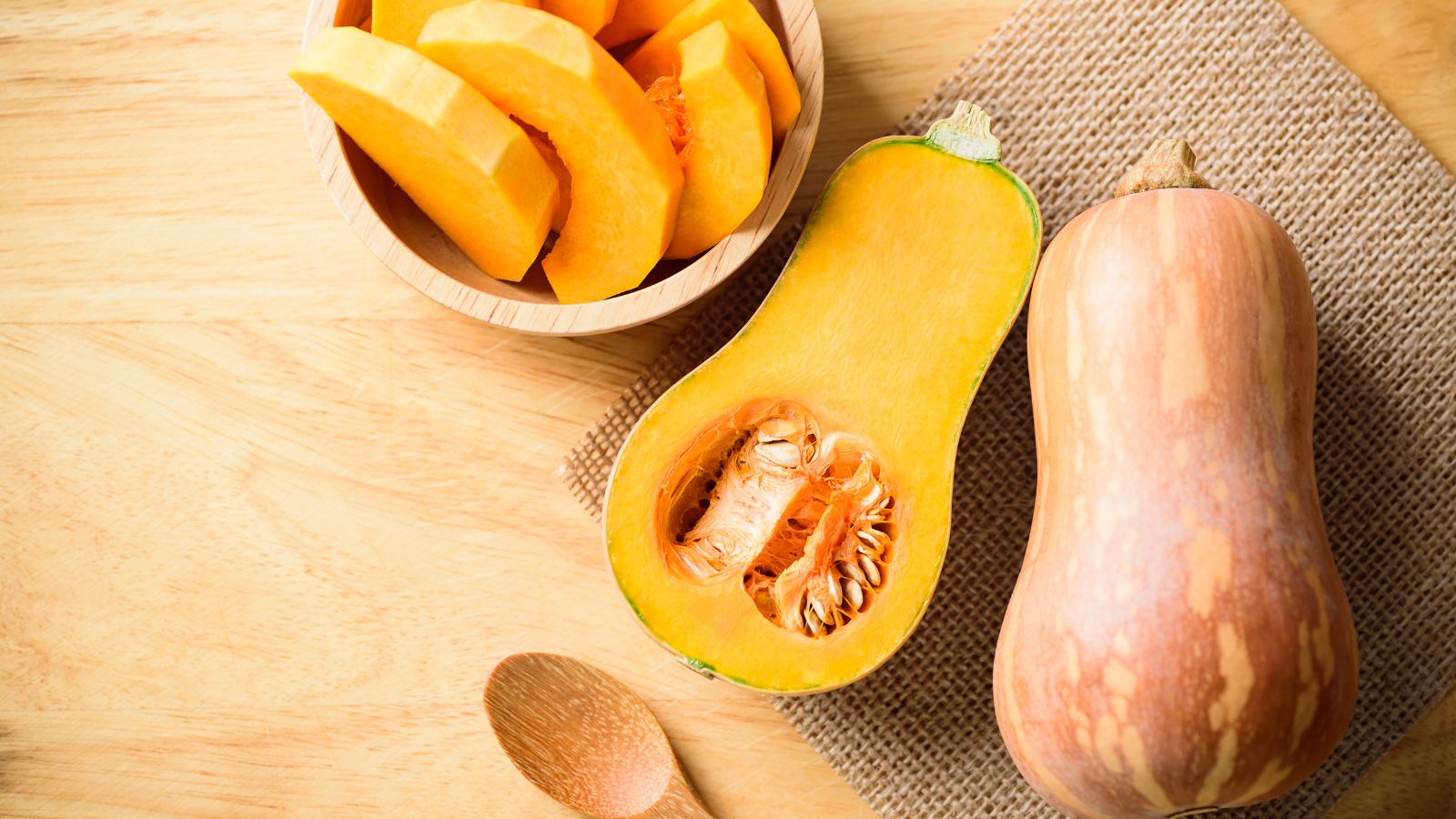 Sliced and whole butternut squash on wooden surface.