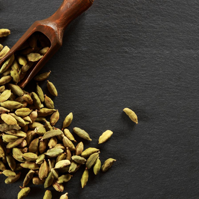 Cardamom pods scattered on a dark slate background with a scoop.