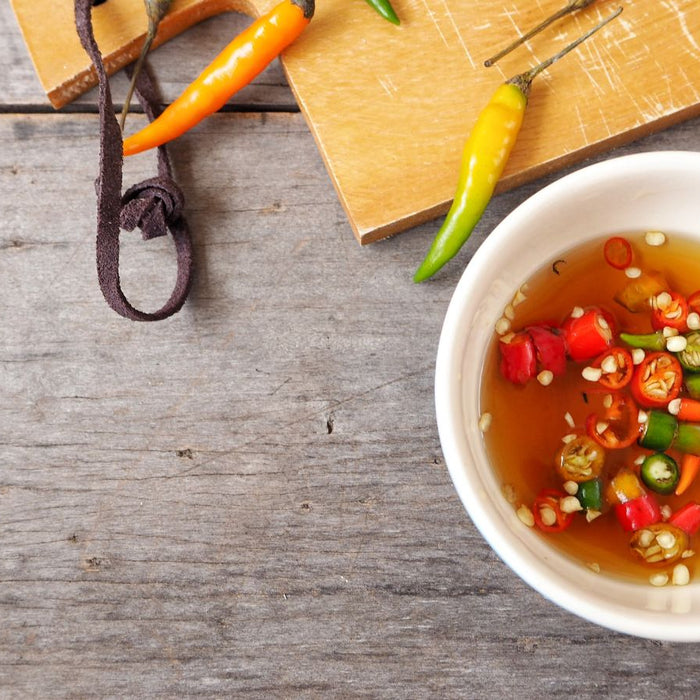 Chili fish sauce in white bowl on wooden table with peppers on side.