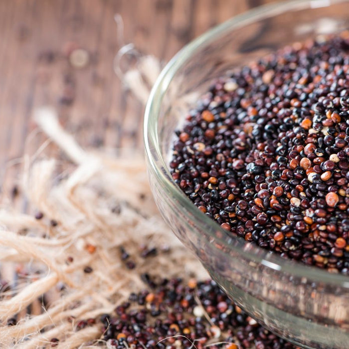 Glass bowl filled with black quinoa on a rustic wooden surface.