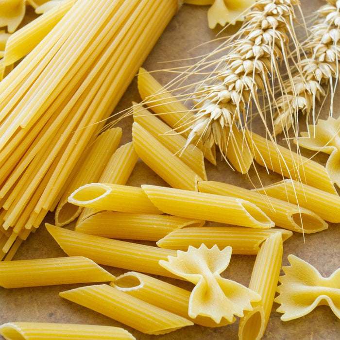Various pasta shapes with wheat on a brown surface background.