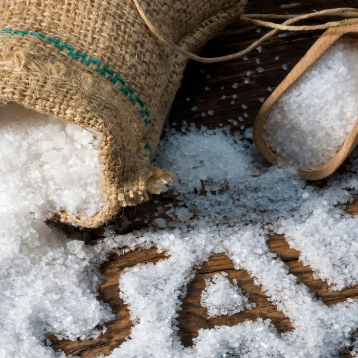 Coarse sea salt spilling from a burlap sack onto a wooden surface