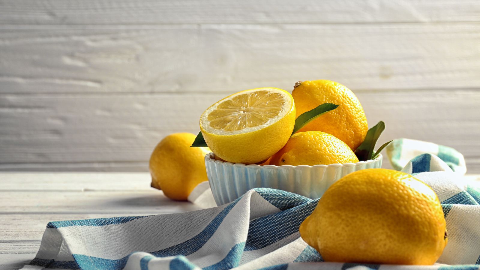 Fresh lemons in a bowl with half cut lemon on striped kitchen towel