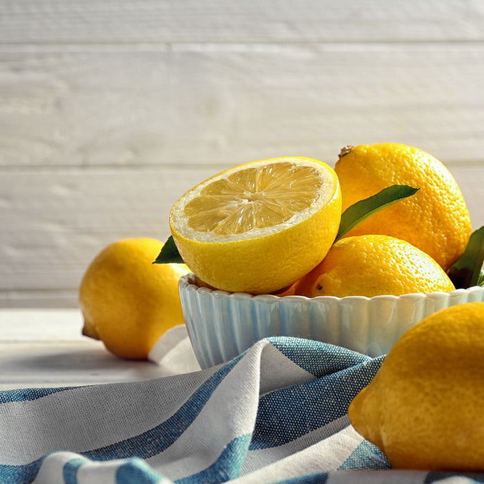 Fresh lemons in a bowl with half cut lemon on striped kitchen towel