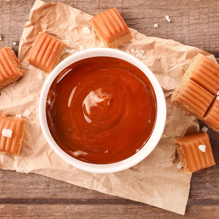 Bowl of caramel sauce with salted caramel fudge on paper wrap.