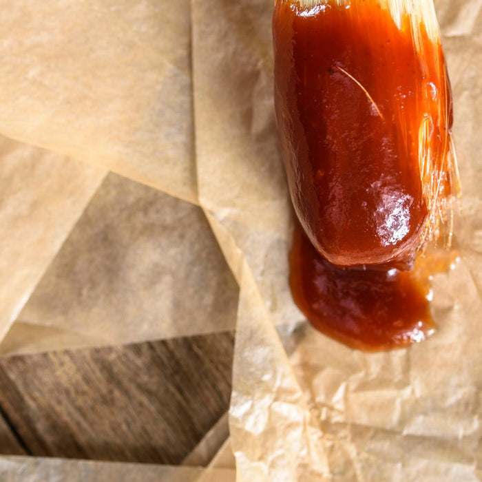 BBQ sauce spread on parchment paper with a basting brush.