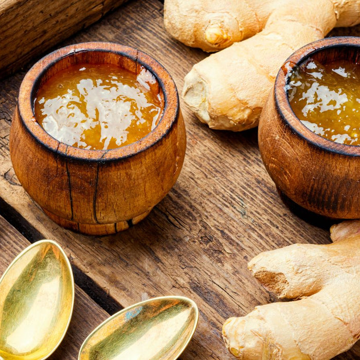 Ginger honey in wooden bowls with raw ginger roots and golden spoons.