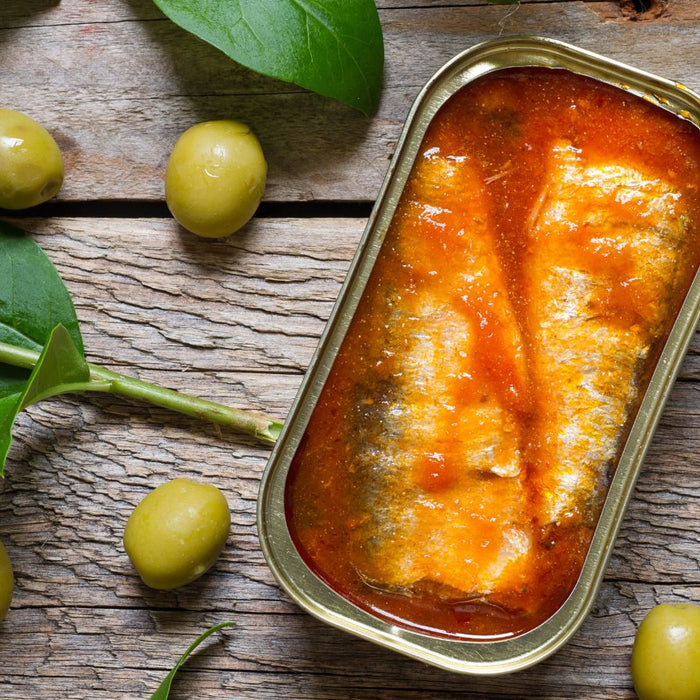 Canned sardines in tomato sauce with green olives and leaves.
