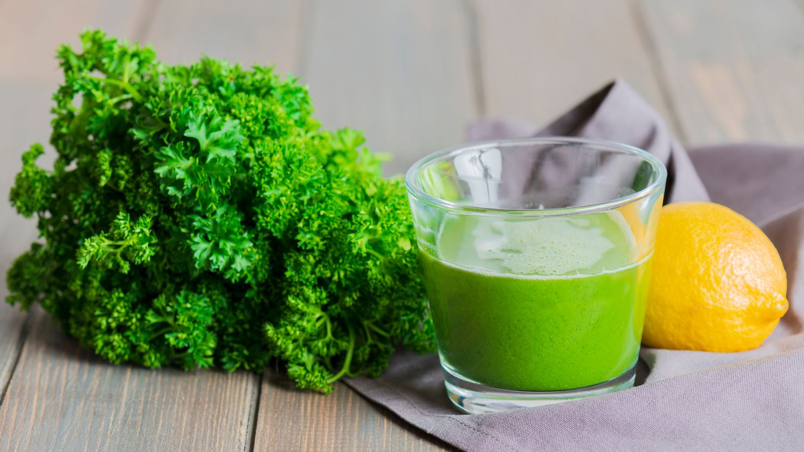 Glass of green juice with parsley and lemon on rustic table.