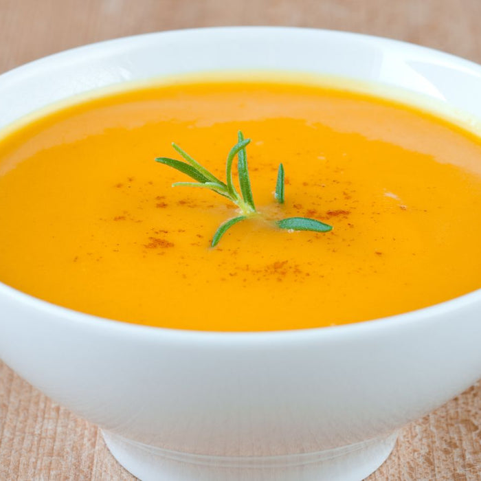 Creamy vegetable soup garnished with rosemary in a white bowl