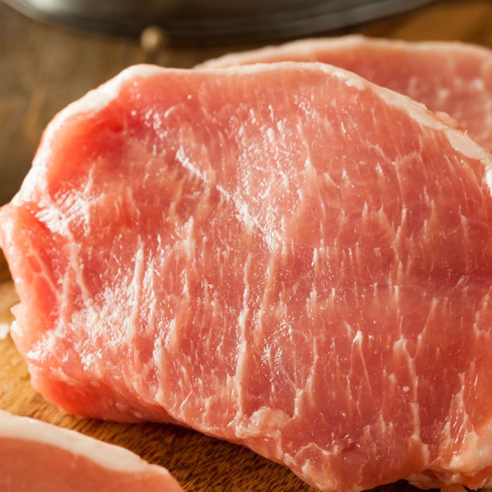 Raw pork chops on a wooden cutting board with salt in the background.