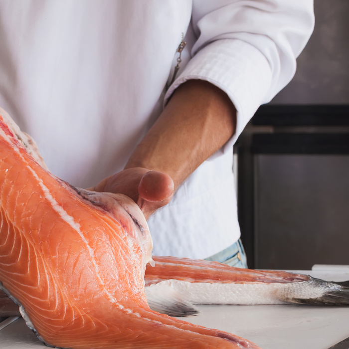 Chef filleting fresh salmon on a white cutting board in kitchen.